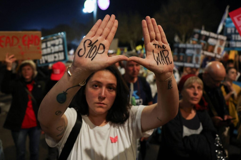 Uma mulher está em um protesto, levantando as mãos com as palavras