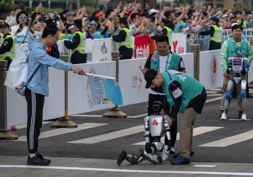 Dois humanos levantando um robô em uma prova de corrida, com um fiscal apontando uma bandeira na cor azul.