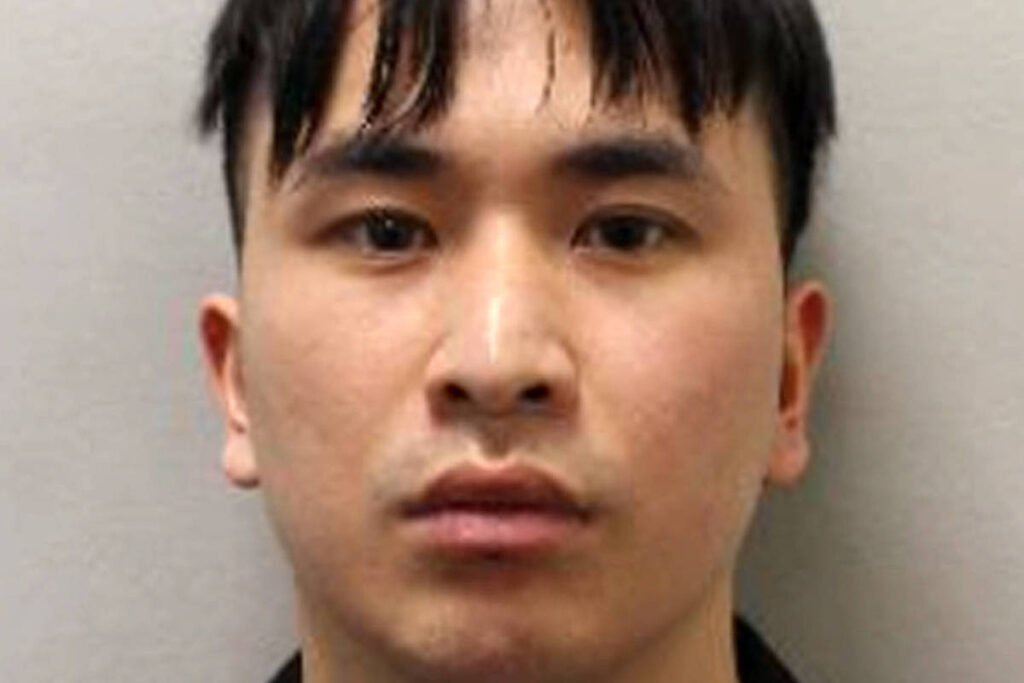 A imagem mostra um retrato de um homem com cabelo escuro e liso, preso na parte da frente. Ele tem uma expressão neutra e está olhando diretamente para a câmera. O fundo da imagem é de cor clara, destacando o rosto do homem.