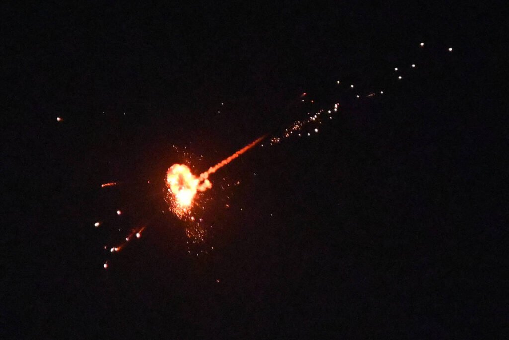 A imagem mostra um fogo de artifício que se assemelha a um coração, com uma explosão central brilhante e faíscas se espalhando em várias direções. O fundo é escuro, destacando o brilho do fogo de artifício.