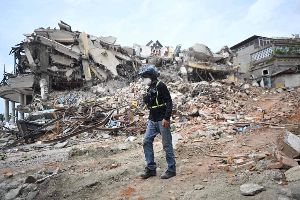 Terremotos na Venezuela: homem salvo após 30 horas Homem com capacete e colete de segurança caminha em terreno de escombros diante de prédio parcialmente destruído.